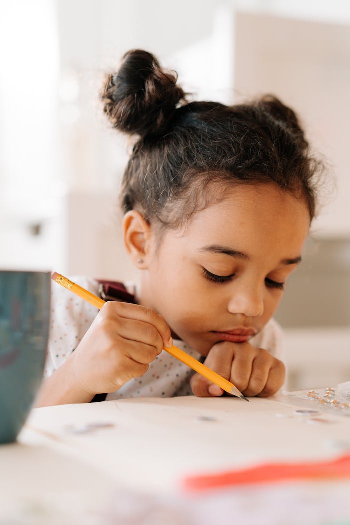 A young girl concentrating on drawing with a pencil inside a bright room, showcasing creativity and focus.