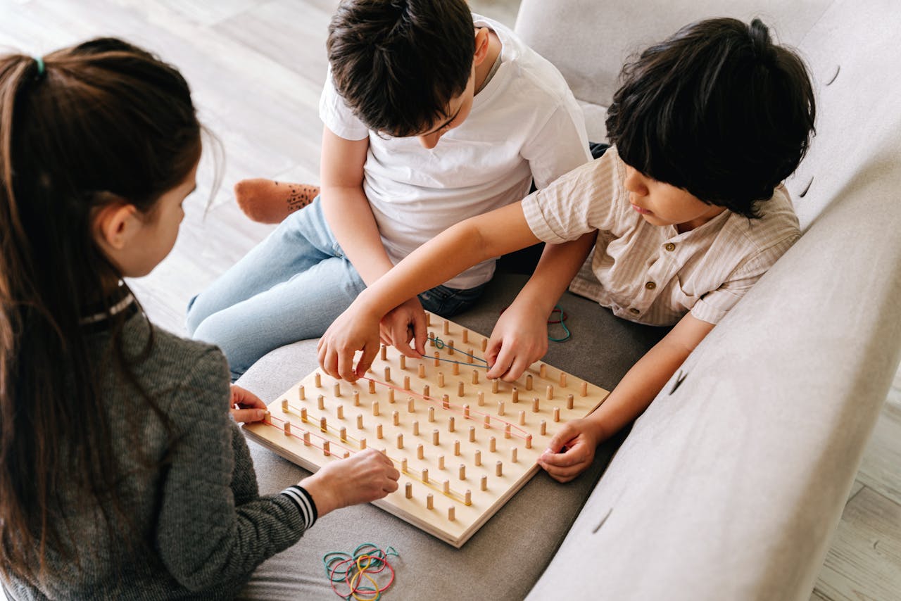 Three children playing with a geoboard, enhancing logic and creativity indoors.